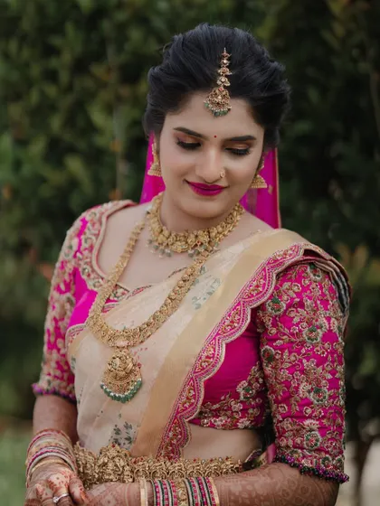 This bride looks absolutely radiant in a cream-colored silk saree contrasted with a vibrant pink blouse. The floral embroidery on the sleeves adds a delicate, feminine touch to her bridal look.