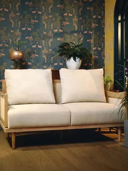 This two-seater sofa combines a light wood frame with cane side panels and plush cream cushions. It's a perfect example of my tailored approach to creating furniture with character.