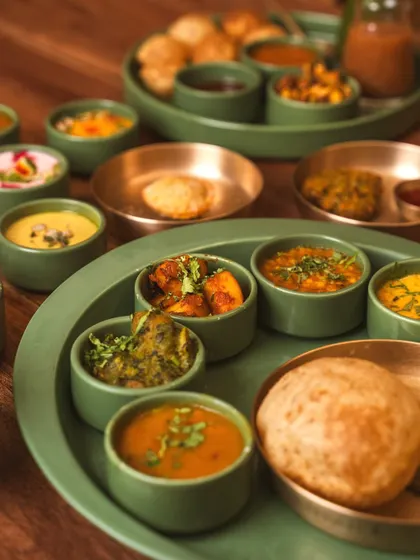 A detailed view of a contemporary Indian thali, focusing on the variety of small bowls filled with different preparations. The composition guides the eye across the different colors and textures.