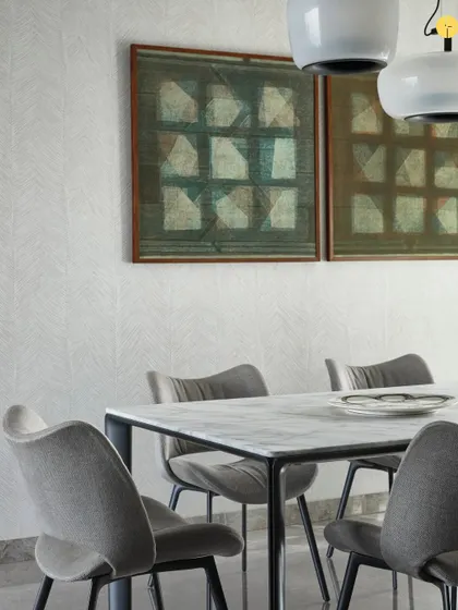 The dining space at 'Pad by the Bay' features elegant chairs and a minimalist table, allowing the focus to remain on the artwork and the view. The wallpaper adds a subtle texture, enhancing the room's quiet sophistication.