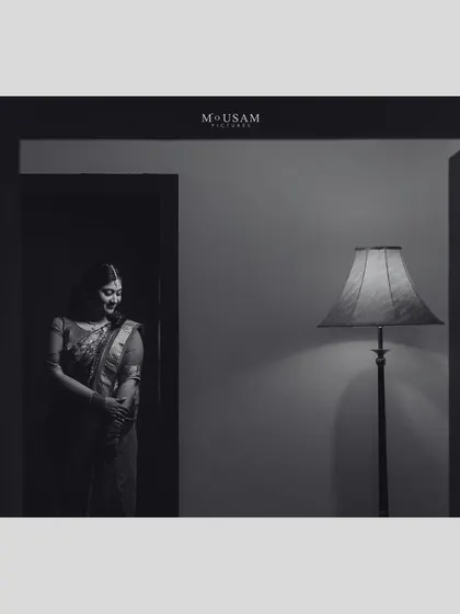 A dramatic black and white portrait of the bride standing in a doorway, illuminated by a single lamp. The play of light and shadow creates a moody, cinematic, and utterly timeless image.