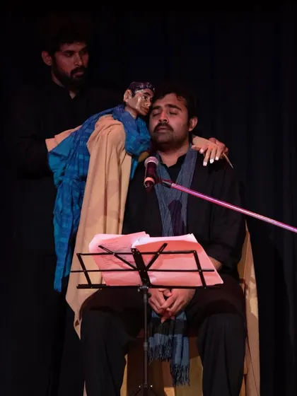 A puppeteer brings a character to life, interacting with a seated musician. This highlights the seamless integration of music and puppetry that is a signature of the 'Buried Treasures' production.