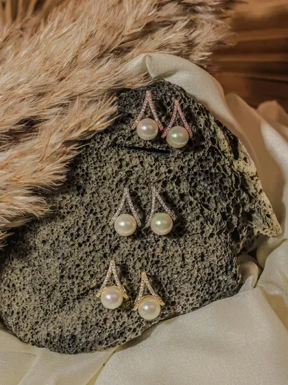 A collection of pearl drop earrings in gold, silver, and rose gold finishes, displayed on a natural stone. This type of shot helps customers compare different color options available for purchase.