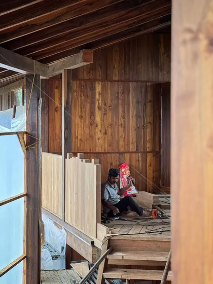 A carpenter takes a moment of rest amidst the woodwork of the farmhouse. The scale and complexity of the timber construction require immense skill and dedication from our team of artisans.