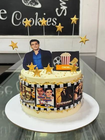 A movie-themed cake for a Salman Khan fan. The cake is decorated with a film strip showing posters of his famous movies and topped with golden stars.