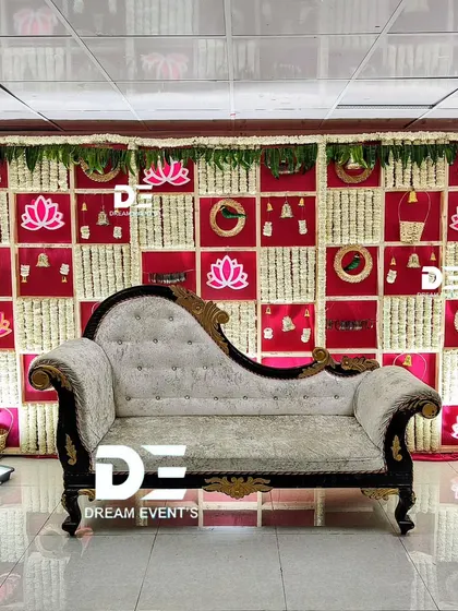 This traditional baby shower backdrop uses a checkered pattern of red fabric panels and tuberose garlands. The design incorporates auspicious elements like bells and lotus motifs.