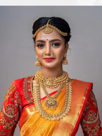 A classic muhurtham look with a yellow silk saree and a red embroidered blouse, accessorized with traditional gold temple jewelry.