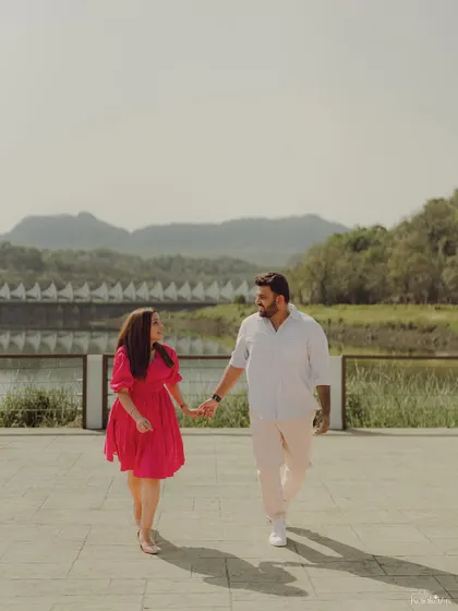 A classic romantic walking shot by the lake, capturing the couple hand-in-hand against a scenic mountain backdrop.