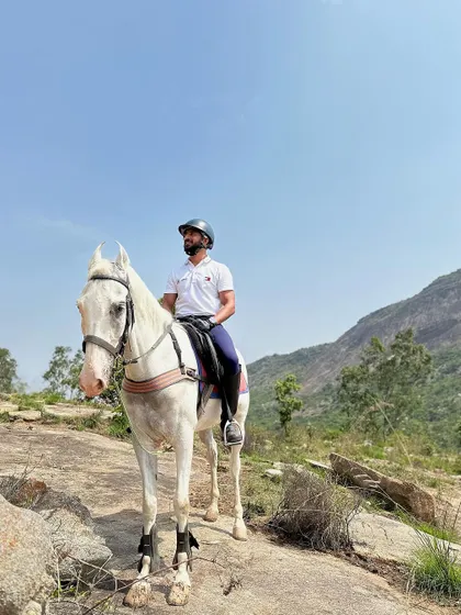 A rider taking a moment to soak in the view from a rocky outcrop on the trail. The white Marwari horse stands steady, a testament to its strength on this terrain.