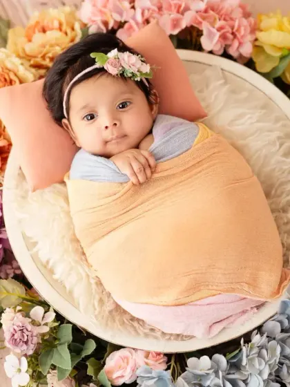 A perfectly wrapped newborn nestled in a floral wreath. Our newborn posing is always done with the utmost care and safety.