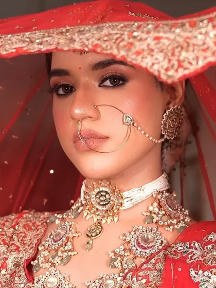 The quintessential bridal shot with a veil. The focus is on the bride's expressive eyes and the stunning nath and choker.