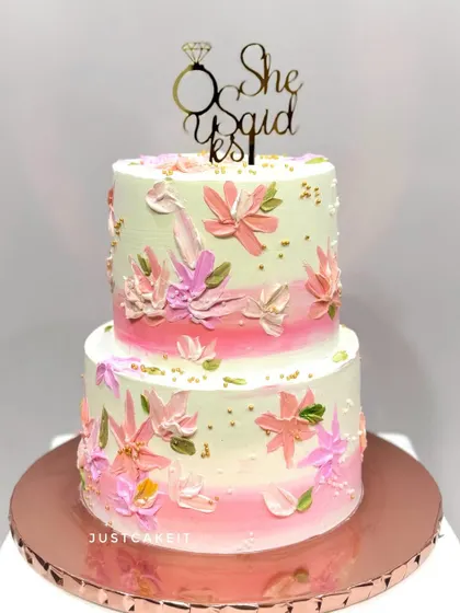 An engagement cake with a "She Said Yes" topper. The design features beautiful, hand-painted flowers using a palette knife technique on a soft pink ombre base.
