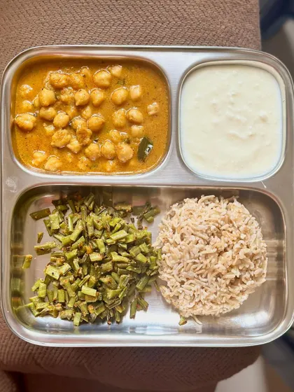 This plate features brown rice, chana masala, sautéed cluster beans, and a side of curd.