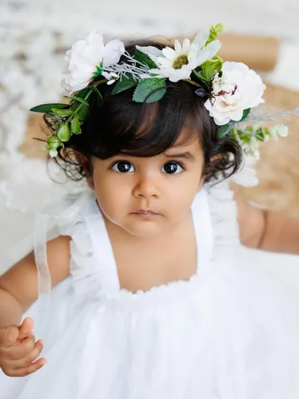 A stunning close-up of a baby girl with a floral headband, her big, beautiful eyes are the focus of this portrait.