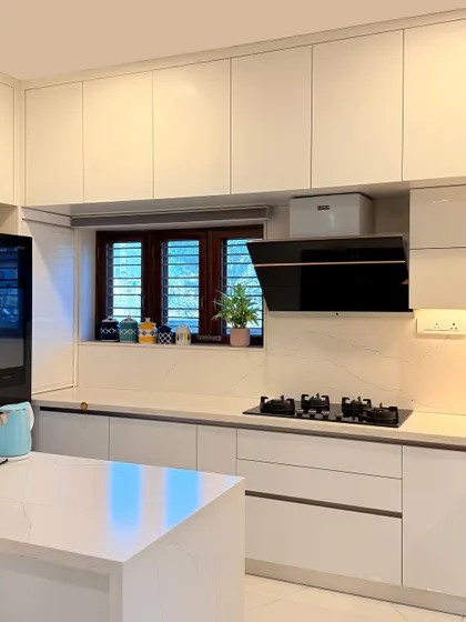 This all-white kitchen in the Haritha and Harinath residence is designed for a clean and timeless feel. The handleless cabinets, built-in chimney, and quartz countertop create a seamless and highly functional workspace.