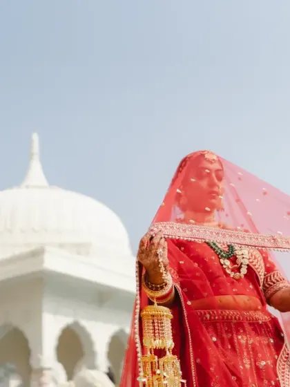 The bride, veiled and radiant, poses against the white marble architecture of the palace. This portrait captures the anticipation and timeless beauty of a bride on her wedding day.