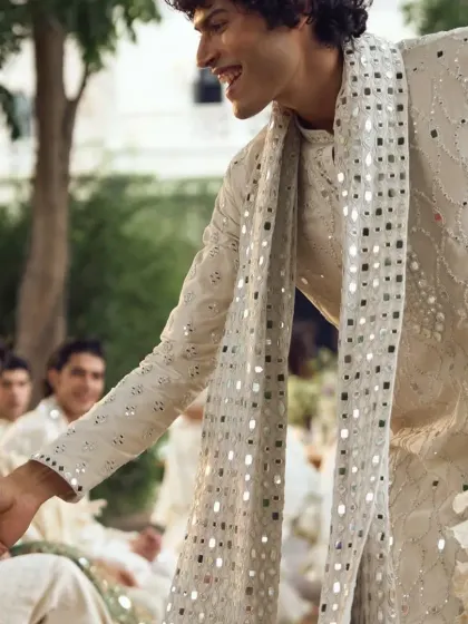 A candid shot from a wedding event, with a guest wearing an ivory mirror-work kurta with a matching stole.