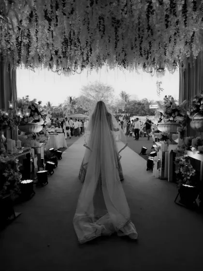 A dramatic black and white photo of the bride walking down a grand, flower-decked aisle.