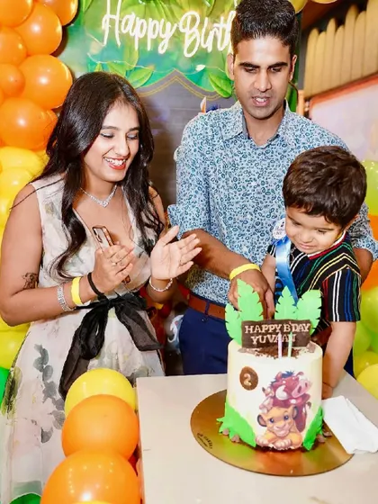 A family celebrates their son's 2nd birthday with a Lion King themed cake and jungle-inspired balloon decor.