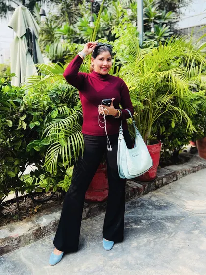 A fall-inspired outfit with a burgundy turtleneck, black flared pants, and a pop of blue from my bag and shoes, set against a green, leafy background.