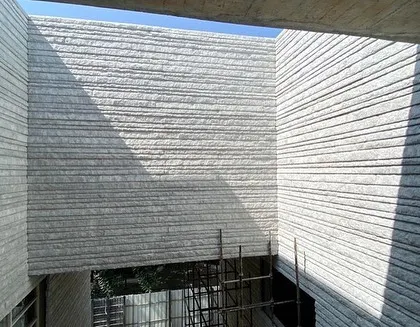 A view of a stone-clad courtyard under construction. The hand-chiseled texture of the stone is designed to catch the light, and the opening to the sky above ensures the space will be animated by the sun's movement.