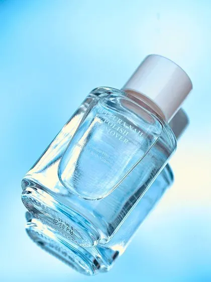 A creative, abstract shot of a nail polish remover bottle. The reflection on a blue, liquid-like surface creates a feeling of freshness and cleansing, aligning with the product's function.