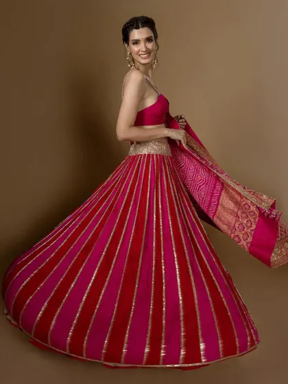 The sheer joy of a twirl in this vibrant pink and red lehenga. The striped kalidar skirt creates beautiful movement, making it a fun and festive choice for a sangeet or garba night.