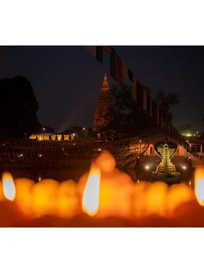 The Mahabodhi Temple is seen at night, framed by the soft, out-of-focus glow of countless butter lamps in the foreground. This composition creates a sense of depth and captures the tranquil evening ambiance.