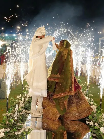 A beautiful varmala moment on a raised mirror stage. The couple is surrounded by an array of cold pyro fireworks, with the sparks reflecting off the stage for double the impact.