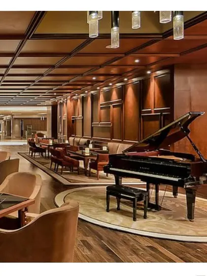 The piano lounge at the Sheraton Bangalore, designed as a sophisticated retreat for guests. The space features rich wood wall paneling, comfortable seating arrangements, and a grand piano as the centerpiece.