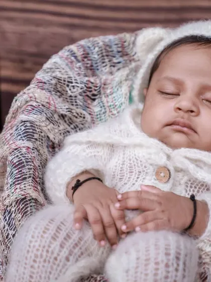 A close-up of the baby in the vintage setup, nestled in a basket with a stack of classic books in the background.