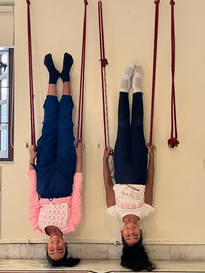 Two young students having fun while building strength with wall-rope inversions. This exercise is great for improving circulation and upper body strength.