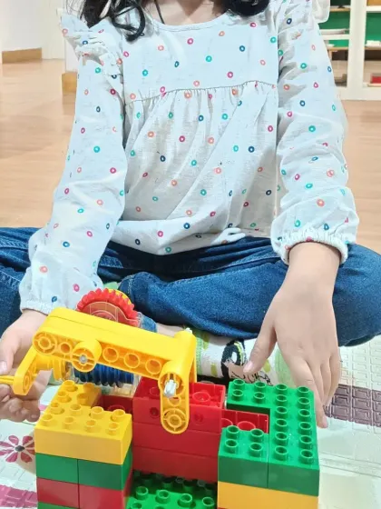 A close up of a young girl working on her LEGO creation. You can see her focus as she connects the pieces, building a simple machine with a moving part.