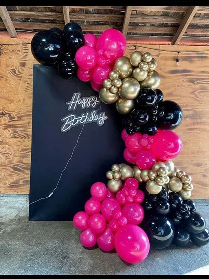 A bold birthday backdrop with a black panel and a neon sign. The balloon garland in hot pink, black, and gold chrome creates a high-contrast, modern look.