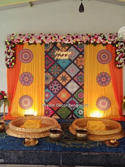 A colorful Haldi backdrop with a patterned fabric centerpiece and a neon "Happy Haldi" sign. The traditional brass urlis for the ceremony complete the look. I was so happy to do this for a repeat client!