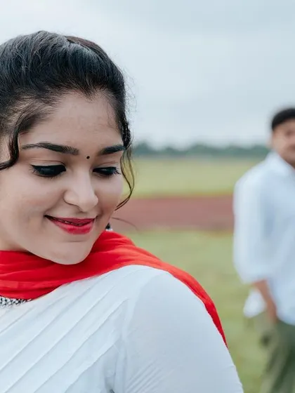 A tender moment with the bride looking towards the groom in the background. The soft focus and natural setting create a dreamy, romantic pre-wedding portrait.
