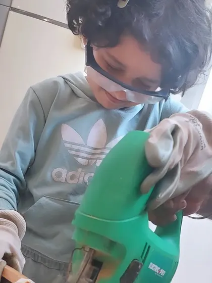 Fully kitted out with gloves and safety glasses, this young builder is learning the fundamentals of woodworking. We believe in teaching real skills in a completely safe setting.