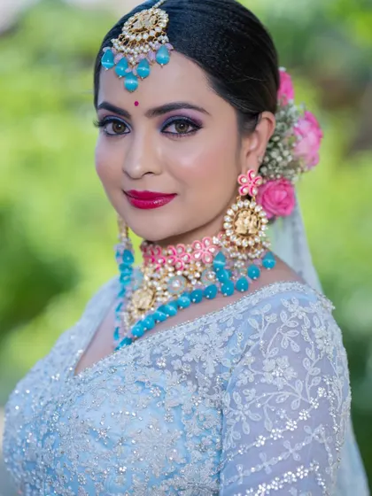 A three-quarter profile of the bride in blue, showing the floral hair accessories and the detailed design of her earrings. The makeup is blended perfectly for a sophisticated finish.