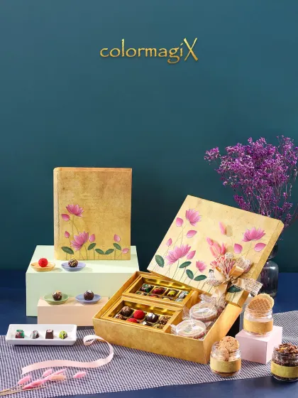 This exquisite golden gift box features a hand-painted lotus motif, blending traditional art with luxury. It opens to reveal a curated selection of fine chocolates and gourmet jar treats.