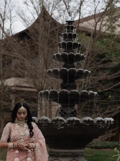 A serene portrait of the bride standing before a fountain, her hands clasped, in a moment of quiet contemplation.