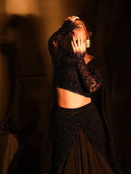 A full-body shot capturing a moment of dramatic movement. The makeup, though not the primary focus, is designed to complement the dark, elegant outfit and adds to the overall moodiness of the image.