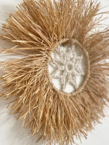 An angled view of the raffia and macrame wall hanging. The natural fibers create a sunburst effect that is both minimal and eye-catching.