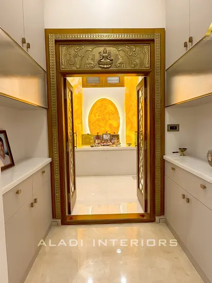 A direct view of the puja room entrance, framed by custom-built, handleless white cabinets with internal lighting, offering a modern and clean storage solution.