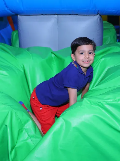 A boy smiles as he climbs over a green inflatable obstacle, ready for his next adventure.