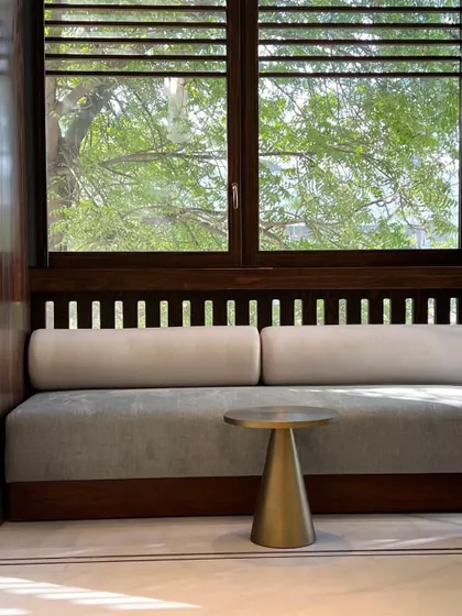 A seating nook by a window, where the design of the furniture and the architectural details work in harmony. The space is framed by greenery, making it a perfect spot for reading or conversation.