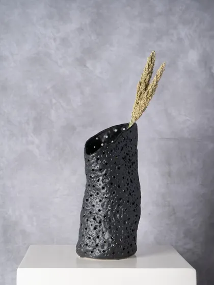 The Ebony Ceramic Vase has a porous, lava-rock texture that gives it a grounded, earthy presence. It is designed to anchor a styling setup with its quiet drama, shown here with simple dried wheat stalks.