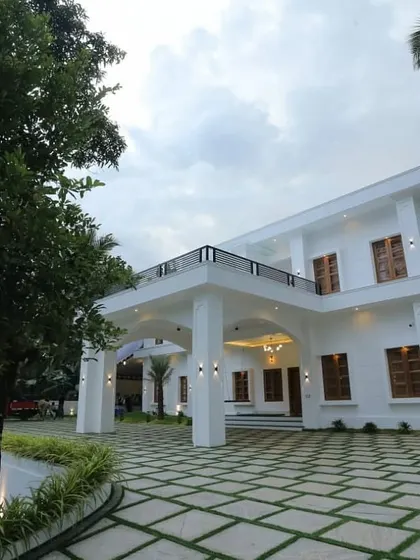 A view of a modern white villa where our landscaping provides a clean, structured look. The design features a geometric paver driveway with grass joints, neat garden beds, and mature trees that frame the home's impressive facade.