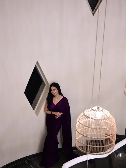 A high-angle shot of me in a deep purple saree, leaning against a wall. This creative angle highlights the modern architecture and the sleek saree.