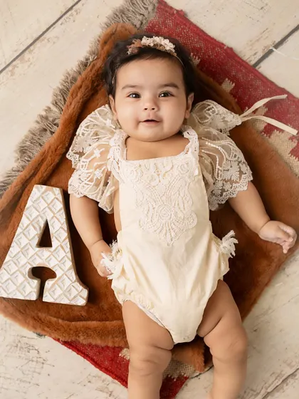 A is for Adorable. This baby girl, in a lacy romper, poses sweetly with her initial for a personalized milestone photo.