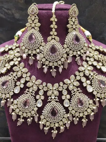 This elaborate silver-toned necklace set features intricate floral motifs with pastel purple stones. It's a unique choice for a reception or engagement and is available to rent as a complete set with earrings and maang tikka.